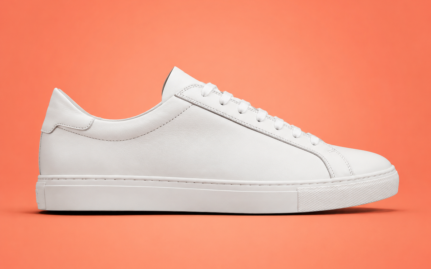 Original product photo of a white sneaker on coral background before AI background removal